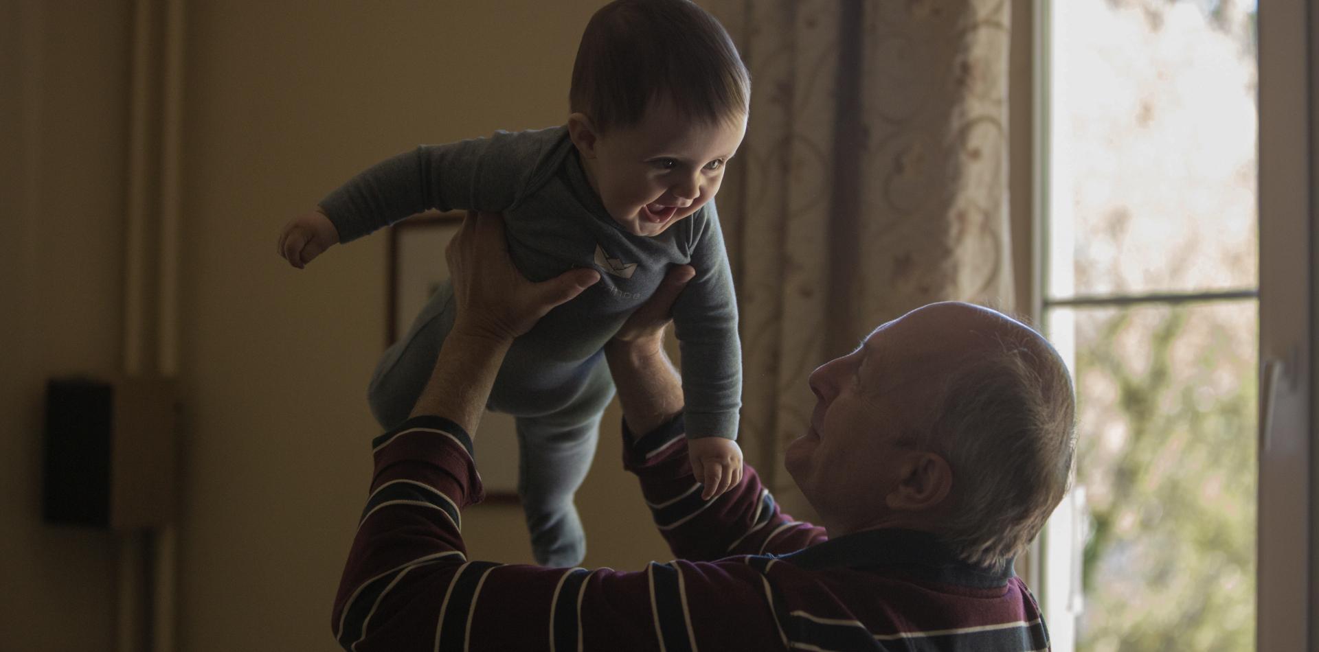 Opa en kleinzoon Een opa die zijn kleinzoon voor een raam omhoog houdt.